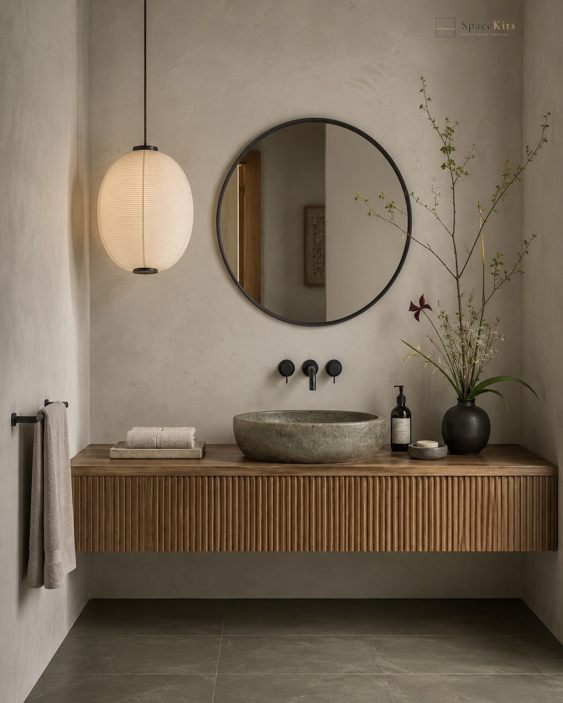 A modern floating bathroom vanity with a slatted wood cabinet, a stone vessel sink, a round black-framed mirror, and a hanging paper lantern pendant light in a minimalist bathroom setting.