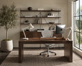 A modern home office with a large walnut desk facing built-in shelving, a white ergonomic office chair, desktop monitor, olive tree in a planter, and sunlight streaming through tall windows.