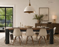 A modern dining room scene featuring a rectangular wooden dining table with dark block legs, surrounded by six cream-colored chairs with wooden legs. A large white dome pendant light hangs above the table, and a matching distressed area rug covers the floor.