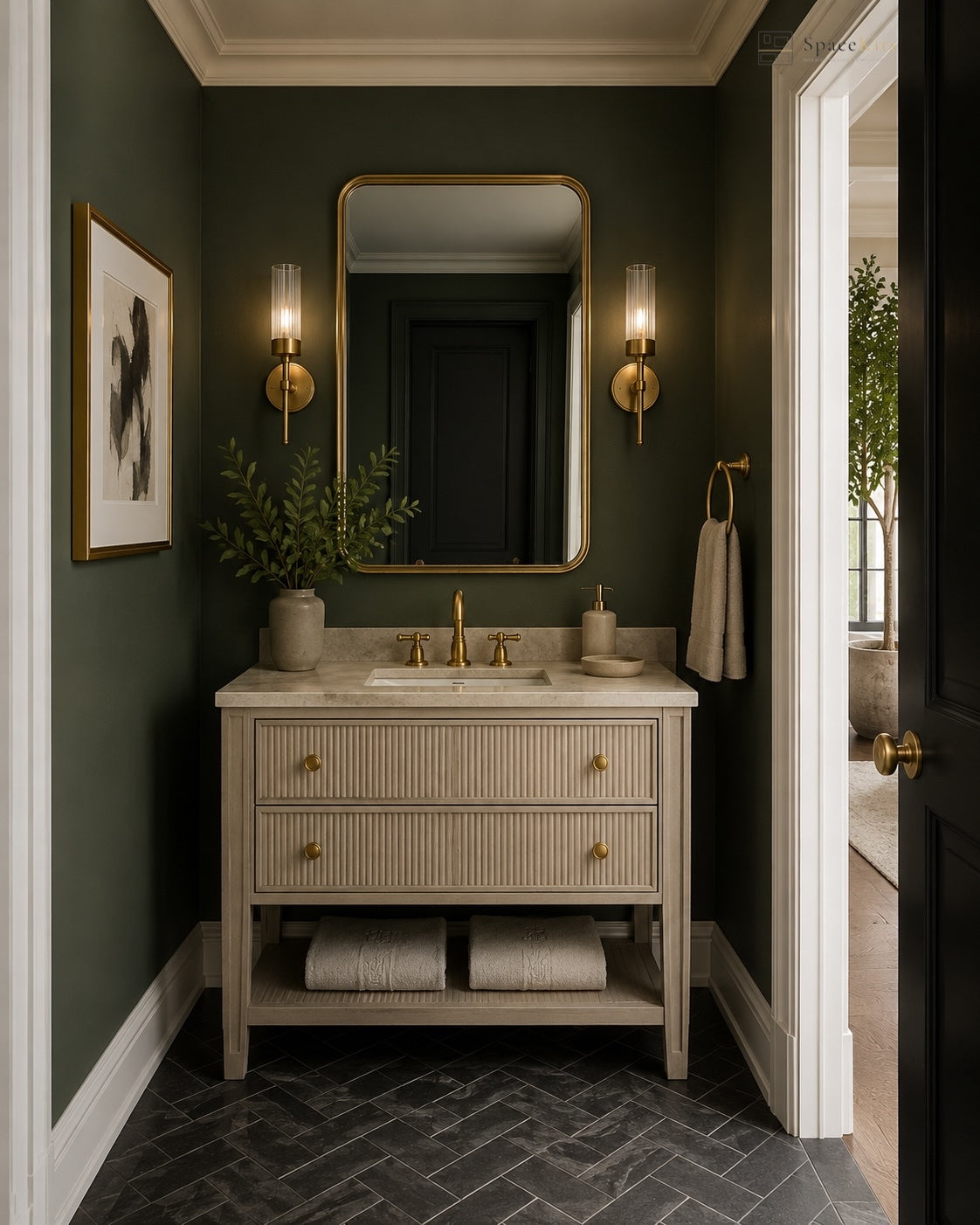 A styled bathroom interior featuring a cream ribbed vanity with a white marble countertop, gold faucets, a large gold-framed mirror, and dark green walls. A framed print, sconces, a plant, and folded towels are arranged around the vanity, with a doorway on the right showing a glimpse of another room.